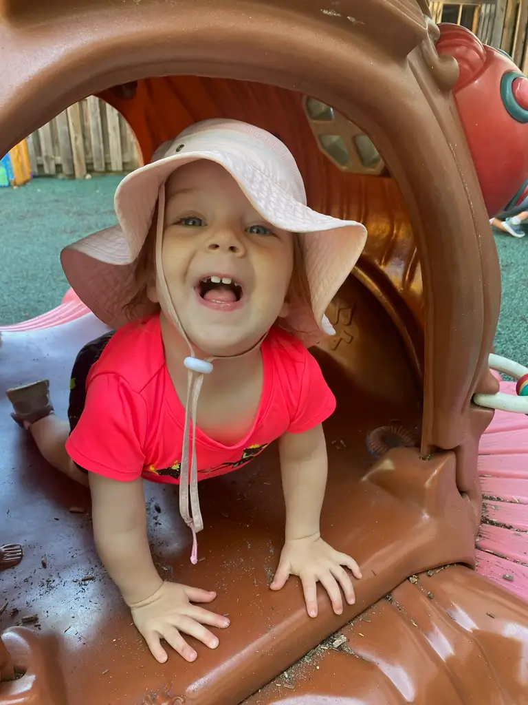 Child playing in playground tunnel, smiling brightly.