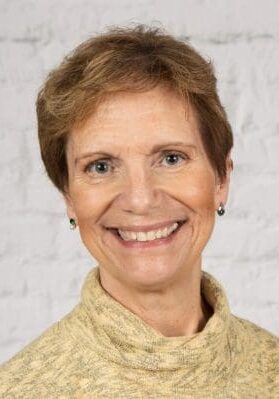Smiling woman with short hair against a neutral background.